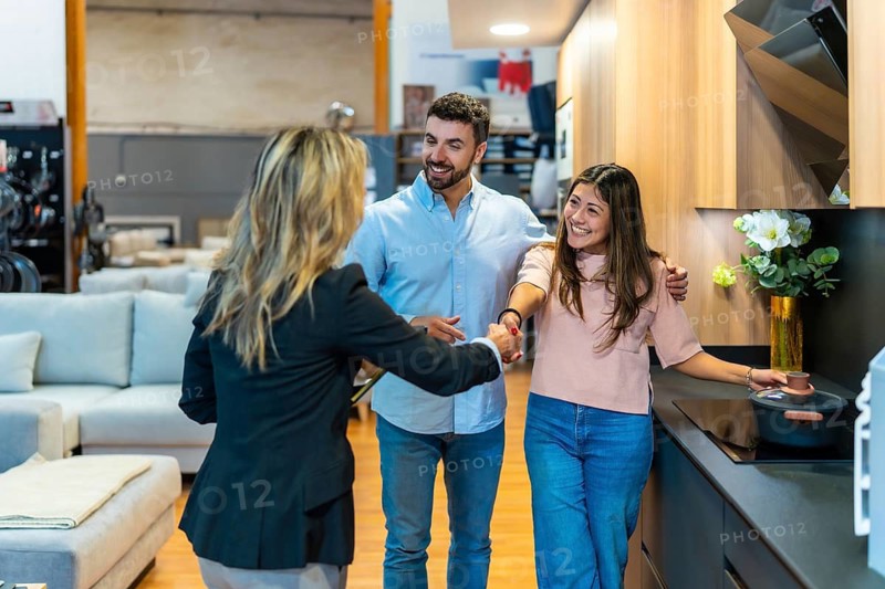 Young couple shakes hands with a sales consultant in a modern kitchen showroom, smiling as they discuss renovation plans, design options and new home improvements