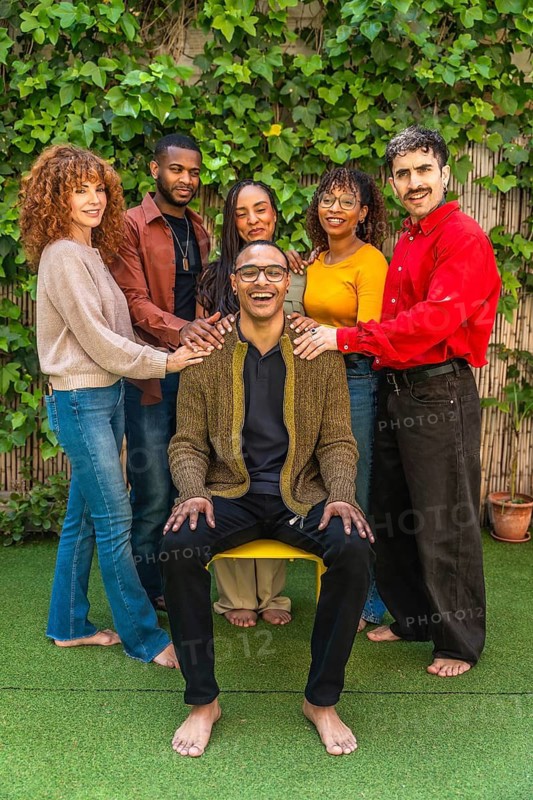 Diverse group of smiling individuals showing unity and mutual support during a therapy session in a green outdoor setting, sharing emotions and fostering connection within a community