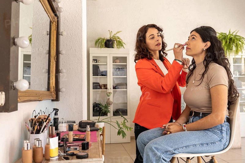 Professional makeup artist applying makeup with a brush to a seated client during a beauty session at a salon vanity station
