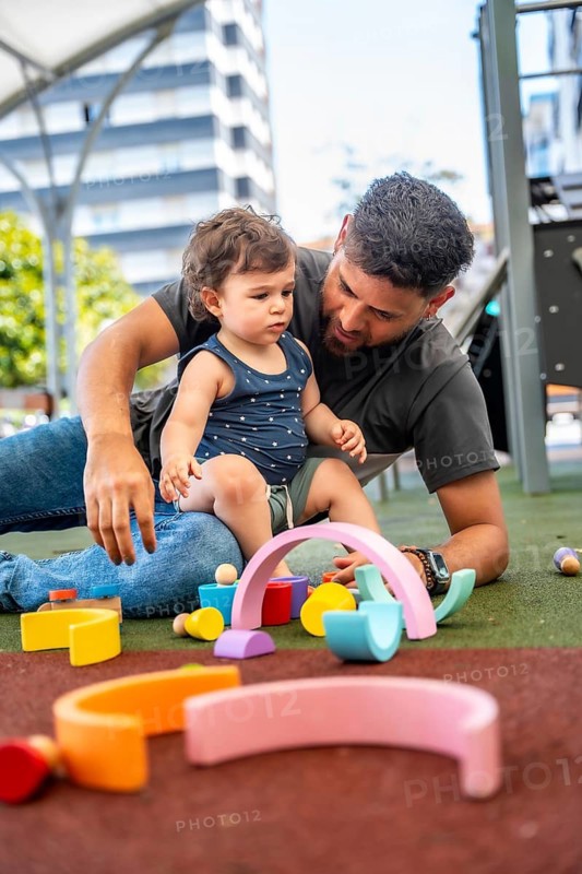 Father and young child enjoying quality time together, playing with colorful wooden building blocks on a playground surface, fostering early childhood development and family bonding