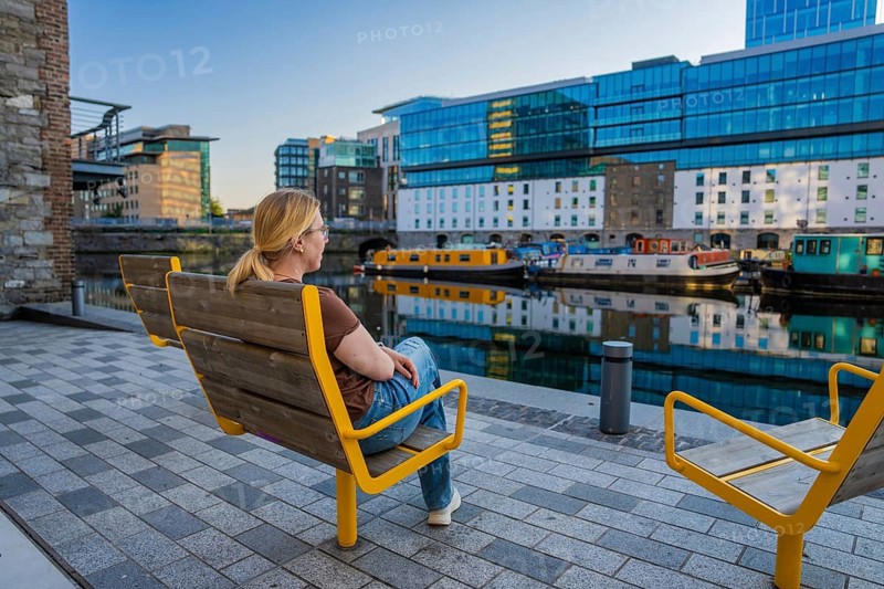 Woman relaxing on waterside benches surrounded by modern architecture and canal boats, Dublin, Ireland