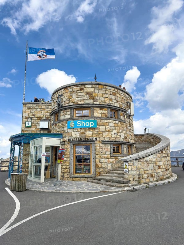 Round observation tower on 2571 meters high Edelweiss peak with flagpole and flag with Grossglockner High Alpine Road motif, souvenir shop in the middle large sign shop, right stairway, Fusch, Salzburg state, Austria