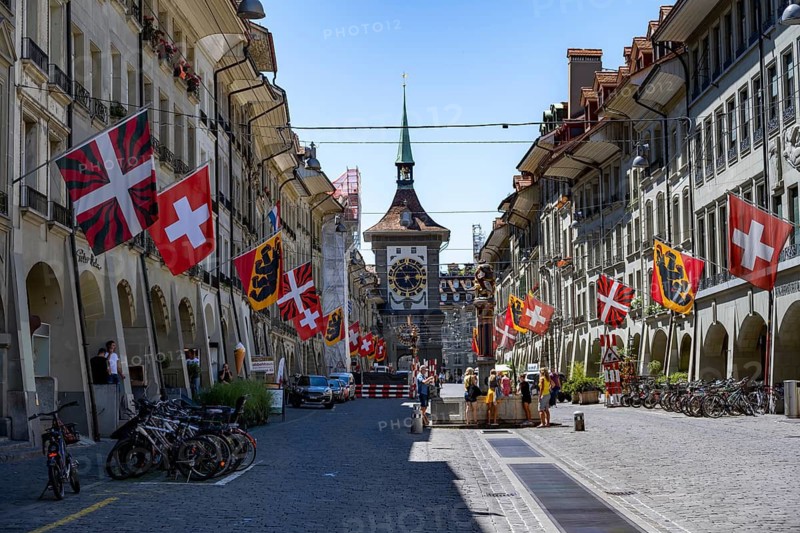 Kramgasse with historic houses and Zähringer fountain, decorated with cantonal flags and Swiss national flags, clock tower Zytglogge in the back, old town, Bern, Canton of Bern, Switzerland