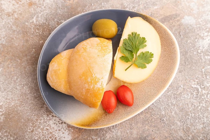 Smoked Mozzarella cheese, with tomatoes and olives on brown concrete background, top view, flat lay, close up