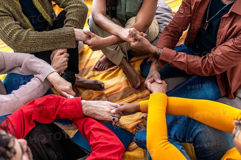 Diverse people sitting together in a close circle, holding hands and showing support, unity, community, and empathy, representing a concept of group therapy and connection