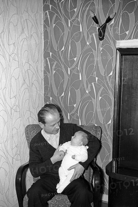 Father sitting in armchair holding baby in arms, Arnsberg, Sauerland, North Rhine-Westphalia, Germany, spring 1962, retro, vintage, old, historic