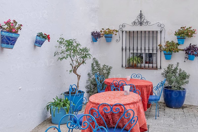 Street cafe with blue chairs and red tablecloths against white walls decorated with flowers, Mijas, Andalusia, Spain