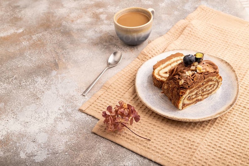 Sweet loaf with cream and caramel, cup of coffee, on brown concrete background with linen beige textile, copy space, side view