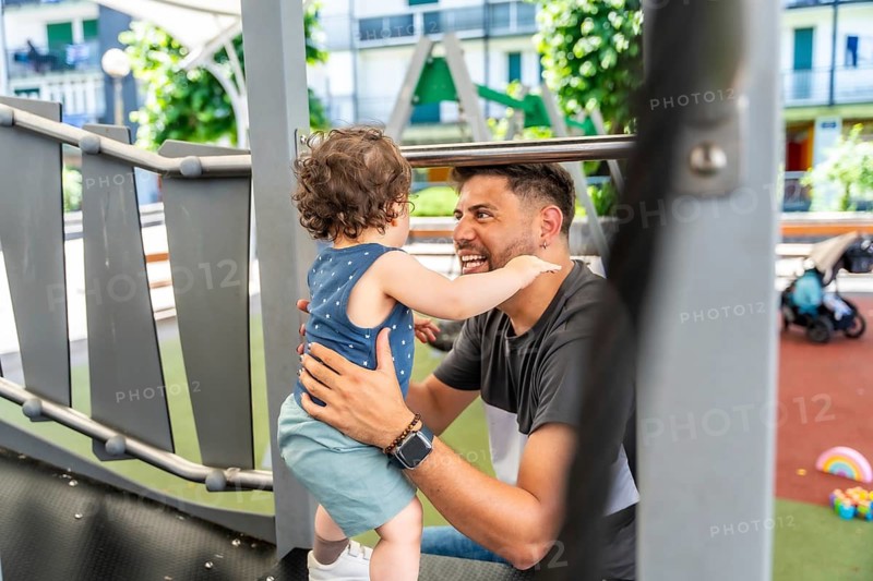 Enthusiastic father bonding with his happy toddler son at a vibrant park playground, sharing a moment of joy and interaction during an outdoor family activity