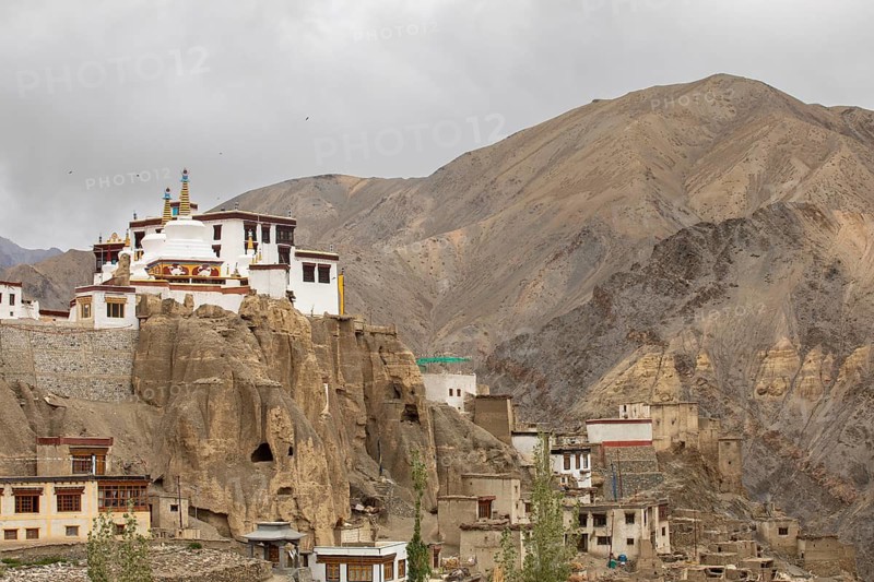 A picturesque view of a monastery perched on rugged cliffs in the serene Zanskar Valley, Ladakh, India. The remote setting is framed by majestic barren mountains