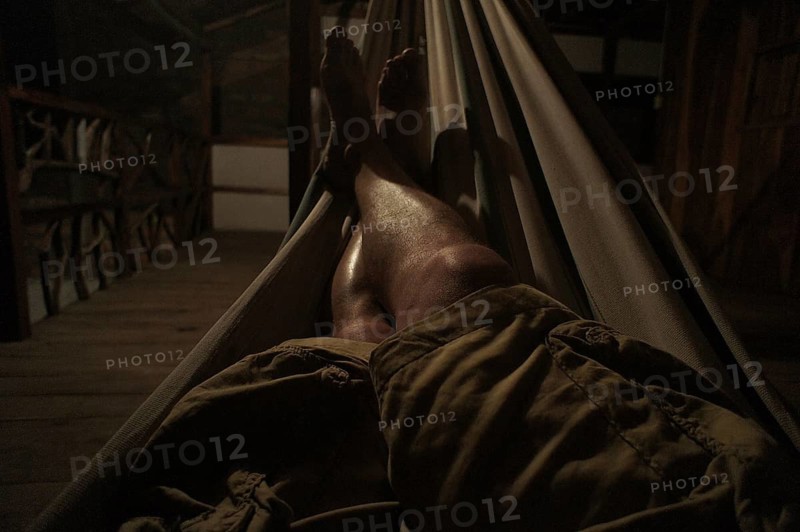Person relaxing in a hammock on a dark wooden veranda, Ecuador