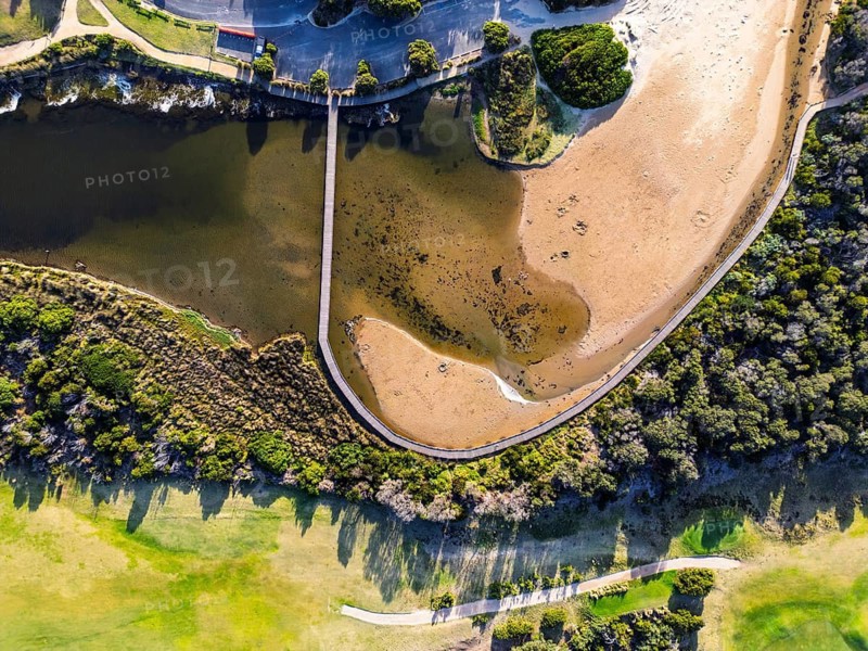 Aerial view of a picturesque coastal landscape featuring green vegetation, a winding waterway and a sandy beach, creating a tranquil natural scene in the Great Ocean Road
