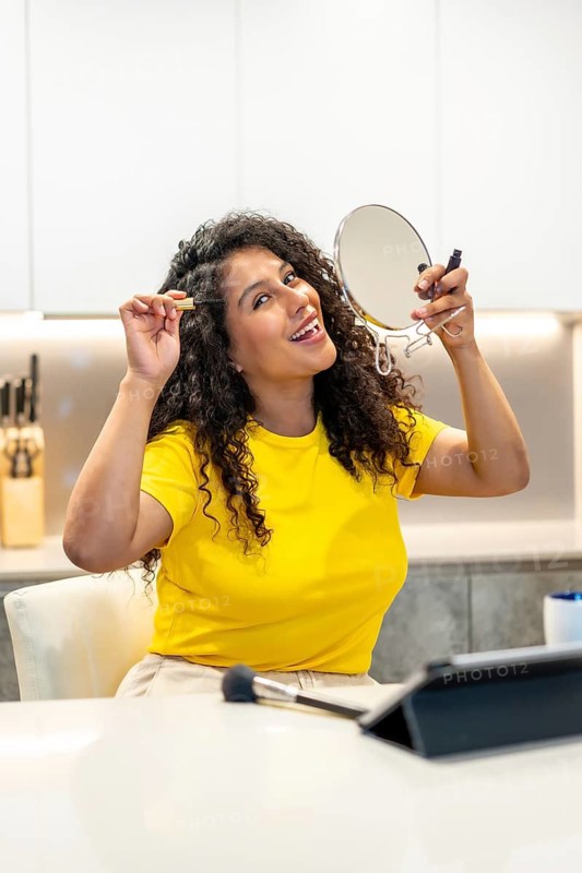 Vertical photo of a happy latin woman making up alone sitting in the kitchen smiling at the camera at home