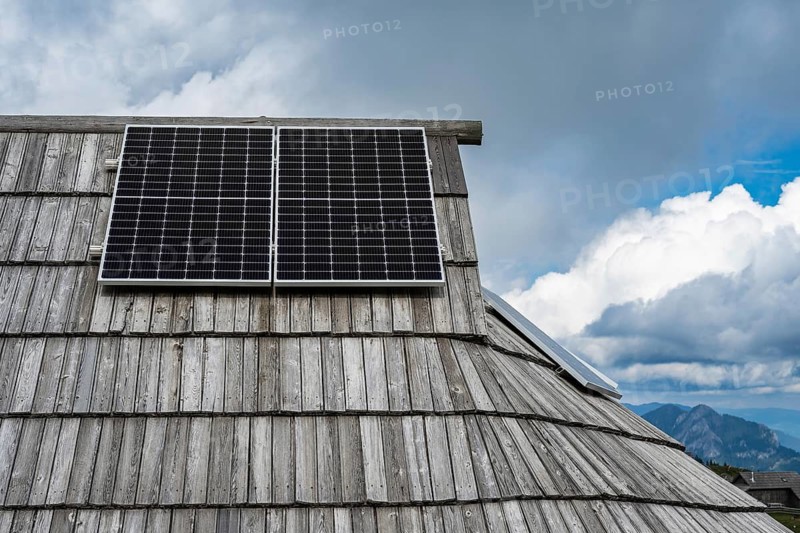 Modern photovoltaic panels installed on the traditional shingled wooden roof of a shepherd's hut against a cloudy sky in Slovenia