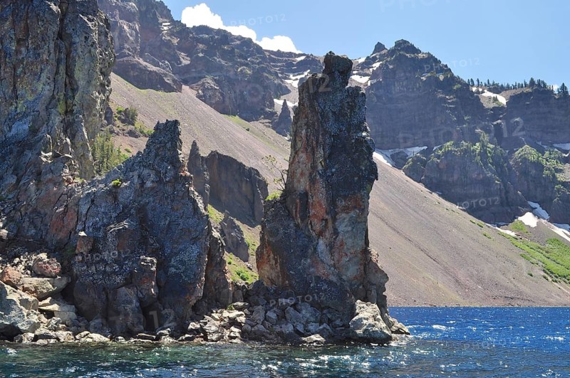 Steep rocks on the edge of a lake with dramatic mountain scenery in the background, Crater Lake National Park, Oregon, USA