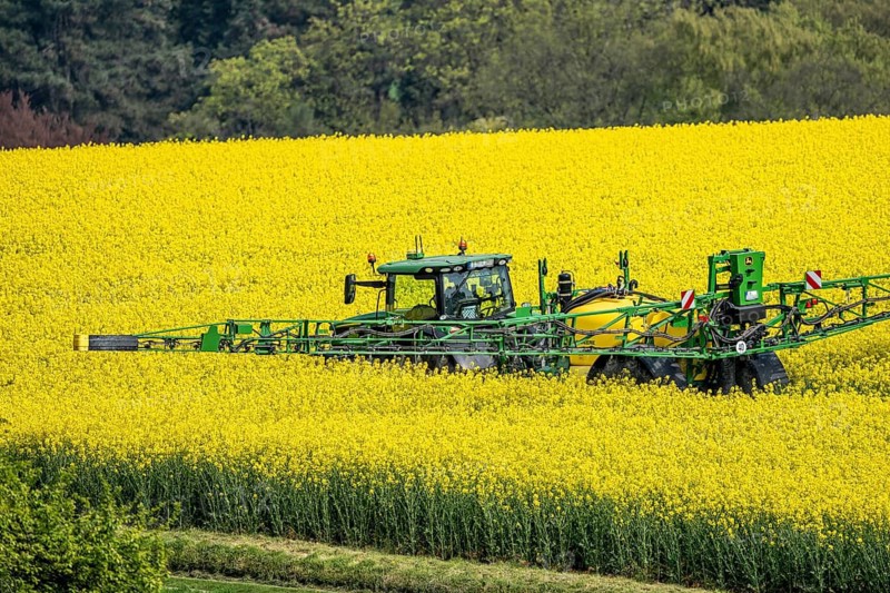 Agriculture, rapeseed field in full bloom, farmer sprays the field with a John Deere M952 trailer sprayer, plant protection products are sprayed against pests during rape bloom, rapeseed is particularly susceptible to pests during flowering, or is sprayed against fungal diseases, fungicides, all products must be compatible with bees, North Rhine-Westphalia, Germany