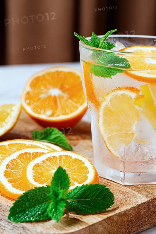 Slices of orange and mint leaves sit next to a clear glass filled with a refreshing drink. The setting is bright and relaxed