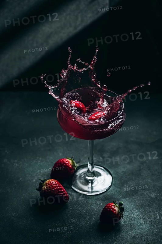 A dynamic image of strawberry liqueur splashing in a glass. Fresh strawberries accent the dark background, highlighting the vibrant red tones of the refreshing drink