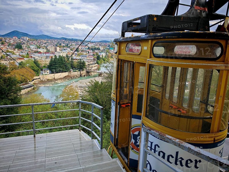 An old cable car with a view of a city, Kutaisi a river and mountains under cloudy sky, Georgia
