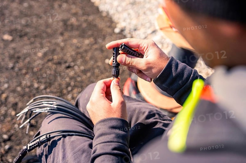 Hands working on a cable connector surrounded by gravel, detailed photo, PV installation at OBI Baumarkt, Mühlacker, Enzkreis, Germany