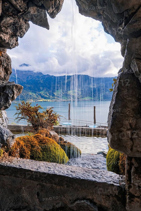 Dramatic view through a rock opening to a waterfall and a lake, St. Beatus Caves, Switzerland