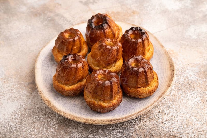 Golden caramelized Canele cookies dessert, cup of coffee, on brown concrete background, close up, side view