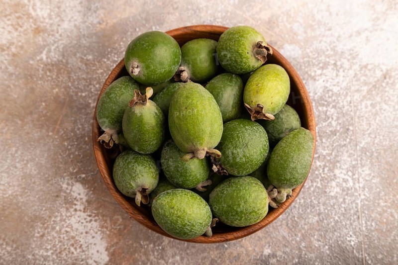 Ripe Feijoa in wooden bowl on brown concrete background, top view, flat lay, close up, minimalism