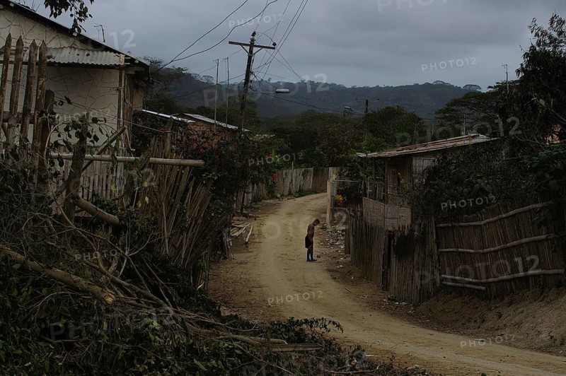 A person on a sandy road in a village with wooden fences, cloudy sky, San Lorenzo, Ecuador