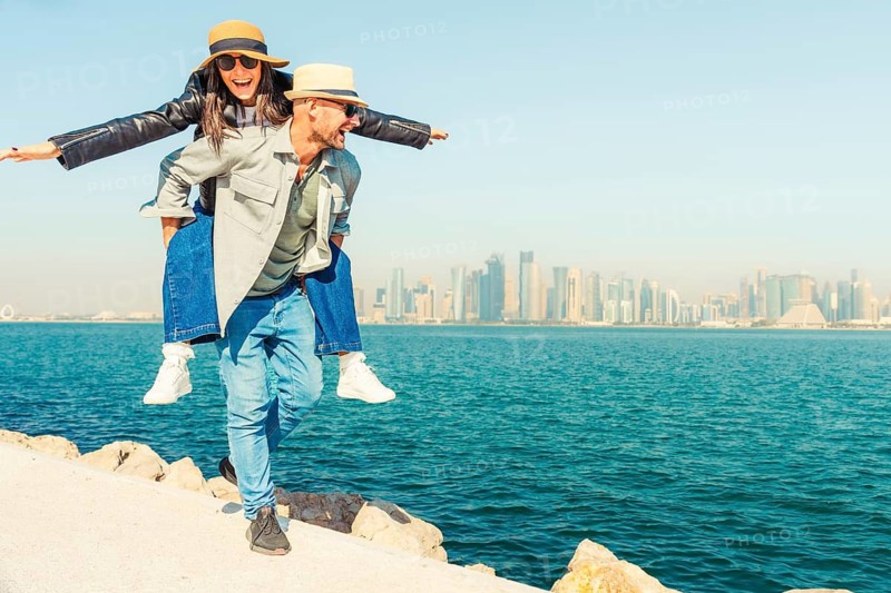 Multiracial beautiful young happy couple of lovers travelers - Multiethnic tourists travelling in middle east and visiting gulf country of Qatar. Doha corniche.Concepts tourism, couple travel lifestyle