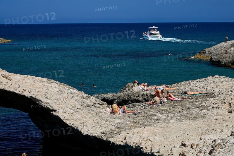 People sunbathe on rocky water's edge while a boat passes by, Kapras, Kapros, Beach, Kapros Beach, Caves, Paralia Kapros, Milos, Cyclades, Greek Islands, Greece