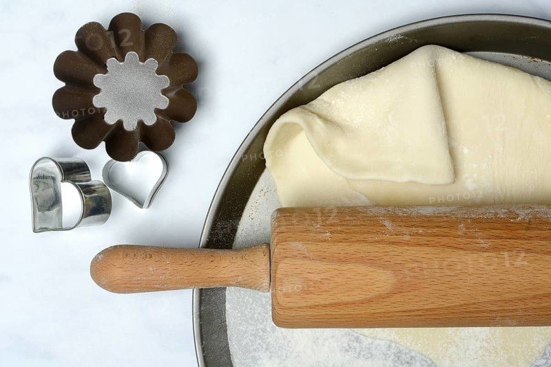 Rolled dough on cake tray with dough rollers and cookie cutters