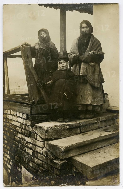 Polish woman, children, Vilnius, poverty, hardship, cold, Lithuania, World War I, two woman and a child standing on a staircase, all wearing warm clothes, atmosphere is subdued, 1916