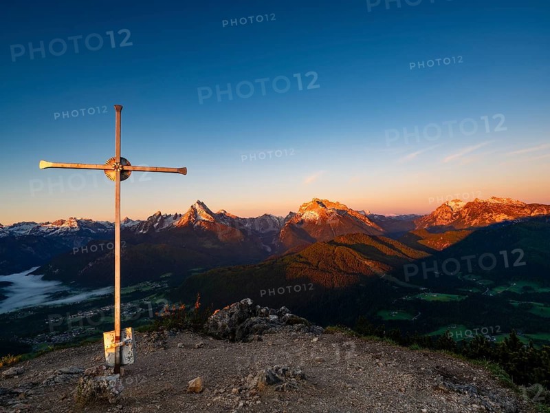 Rauher Kopf summit cross at sunrise, in the background the Berchtesgaden Alps, Steinernes Meer, Schönfeldspitze, Watzmann, Hochkalter and horse-rider Alpe, Berchtesgaden National Park, Bischofswiesen, Berchtesgadener Land, Upper Bavaria, Bavaria, Germany
