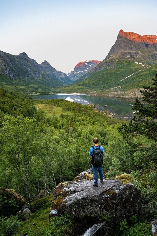 Young man jumping from stone to stone in water, picturesque mountain landscape in the Innerdalen high valley with Innerdalstårnet summit, mountain peaks reflected in Lake Innerdalsvatna, in the evening light at sunset, Trollheimen Mountain Area, Sunndal, Møre og Romsdal, Norway