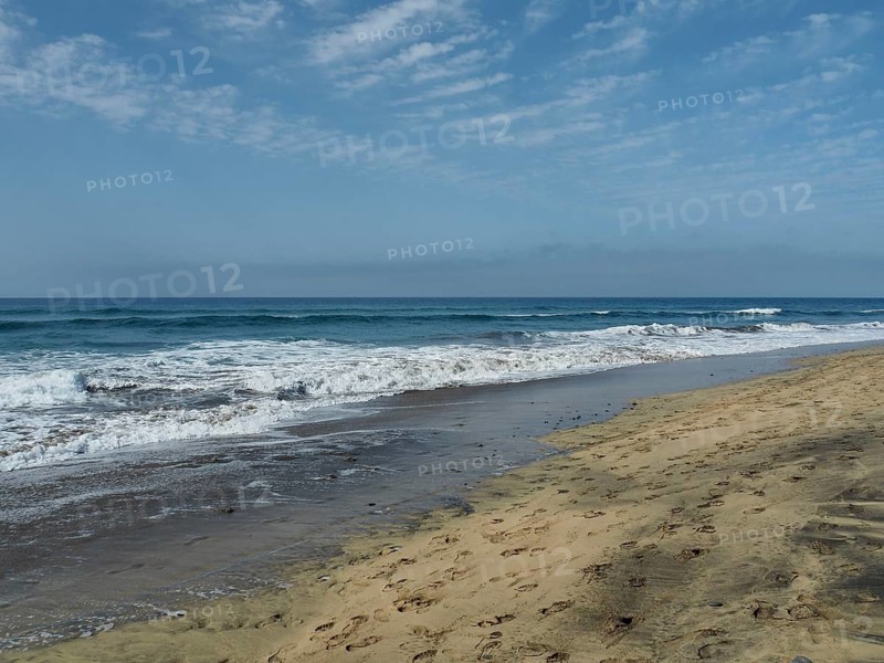 Waves roll in on the beach, footprints run along the water under cloudy sky, Maspalomas dunes, Gran Canaria, Spain