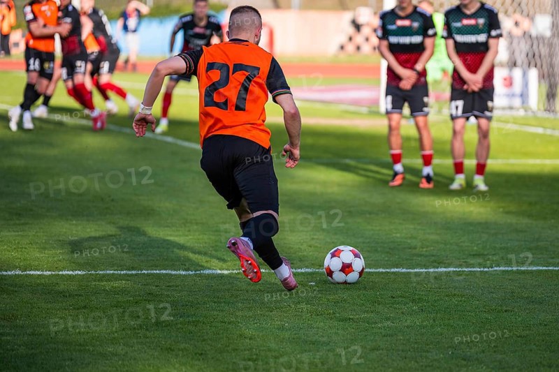 A soccer player in an orange jersey with number 27 runs with the ball toward the opponent's free kick wall during a match in Glogow, Poland