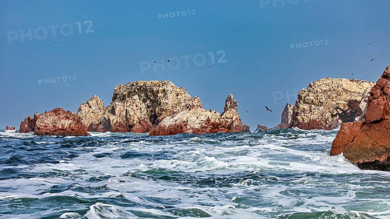 Rock formations in the sea with strong waves under a blue sky, The rocky coast of the Islas Ballestas near Paracas in Peru
