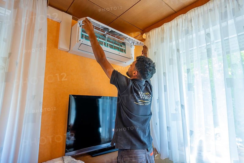 A man installs air conditioning in the living room with television and wooden ceiling, air-conditioning and refrigeration technology, private house, Wurmberg, Germany