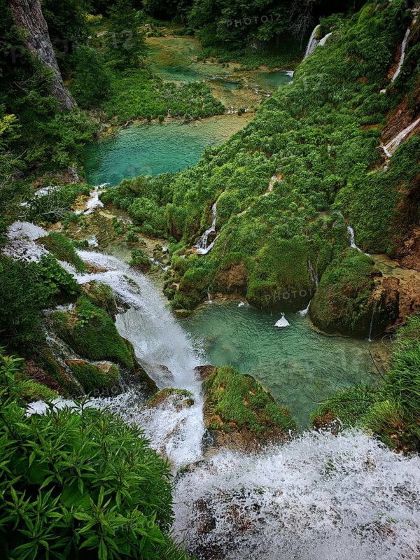 View from above of cascading waterfalls and turquoise-blue lakes amidst thick green vegetation and rocky landscapes, Plitvice Lakes National Park, Croatia