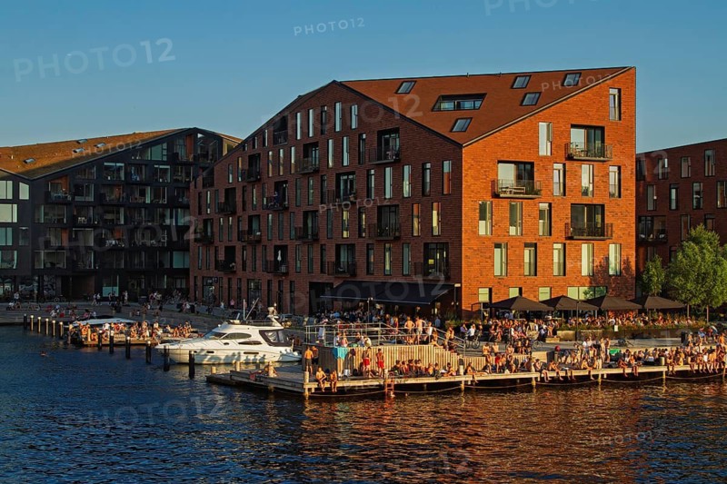 Backsteingebäude bei Sonnenuntergang umgeben von Wasser und Menschen an einem Hafen, Kopenhagen