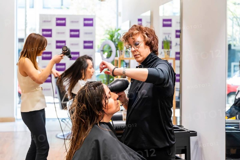 Professional hairstylists providing hair care services to female customers, using hairdryers to dry their wet hair, creating new hairstyles in a modern beauty salon