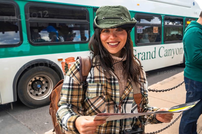 Young woman tourist smiling and holding a park map while waiting at a grand canyon national park shuttle bus stop, planning sightseeing and enjoying the outdoor landscape