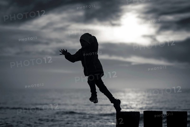 Silhouette of boy jumping from breakwater stilt during sunset