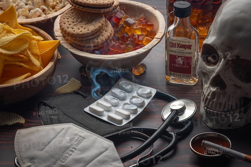 Tablets and stethoscope with skull and crossbones next to unhealthy food and cigarette