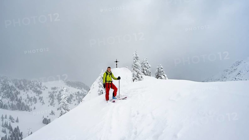 Ski tourers at the summit, summit cross on the Raukopf, mountain landscape in the snow, dramatic clouds, Mangfallgebrige, Bavaria, Germany