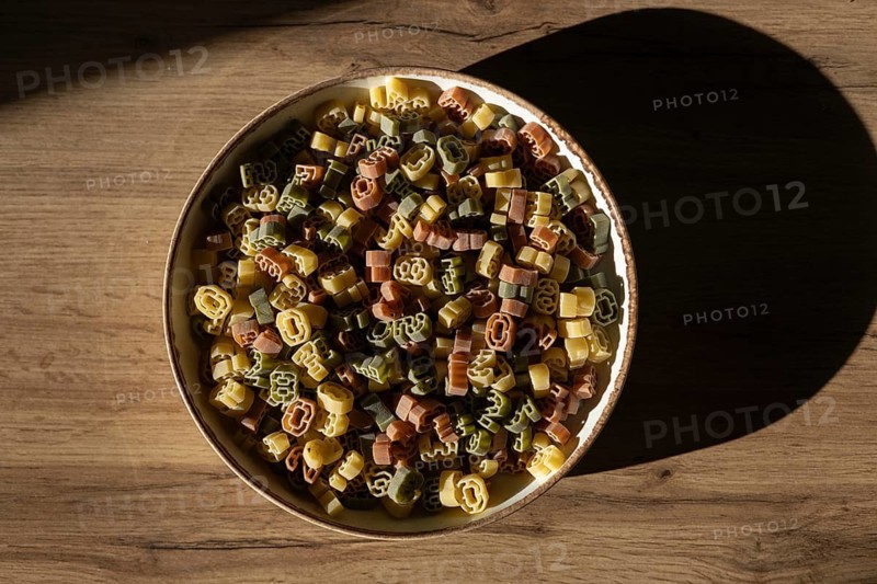 Top view of colorful number shaped pasta in a ceramic bowl, under soft lighting with a distinct shadow on the wooden surface