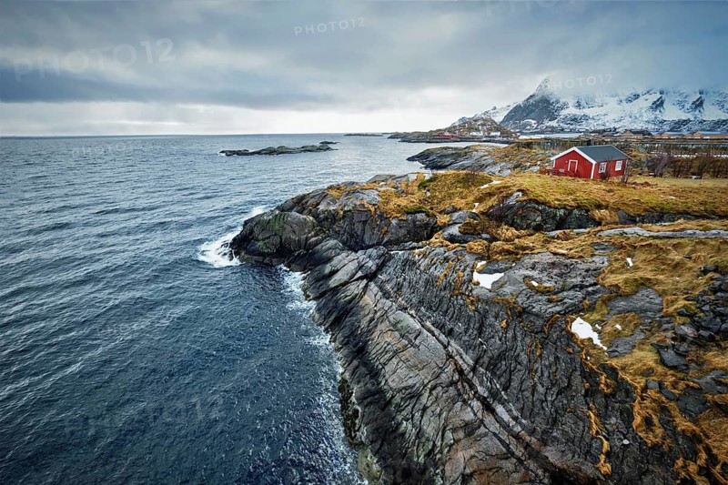 Clif with traditional red rorbu house on Litl-Toppoya islet on Lofoten Islands, Norway in winter