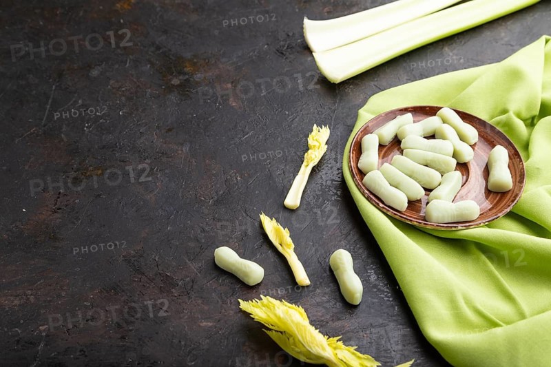 Jelly celery candies on black concrete background and green linen textile. copy space, side view