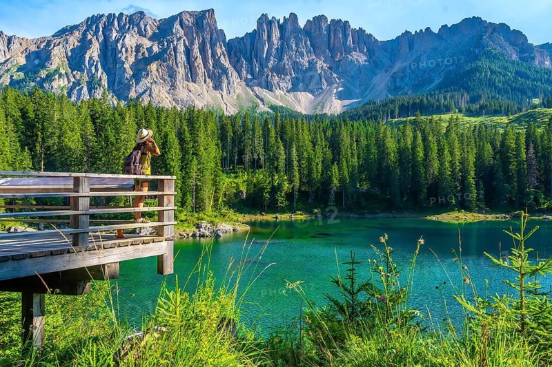 Tourist admiring the stunning landscape of lake carezza with the latemar mountain range in the background, dolomites, italy