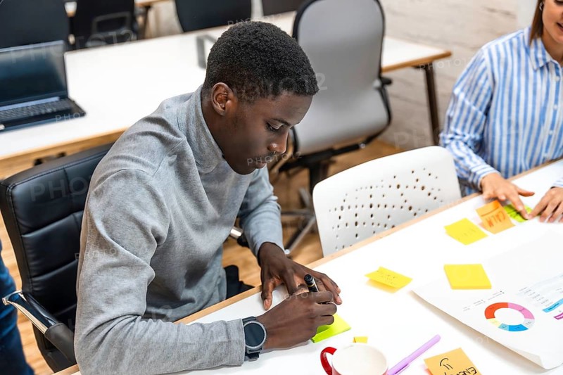 African man writing ideas in a note during brainstorming meeting in a modern coworking